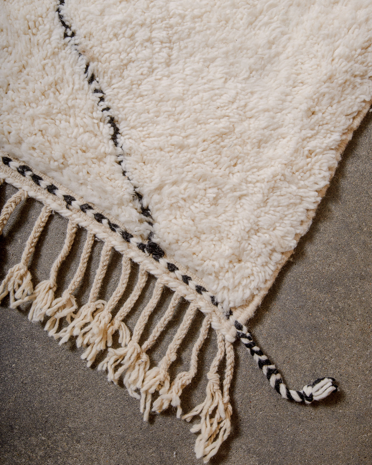Corner of cream Beniourain rug with black diamond design and natural wool tassels.